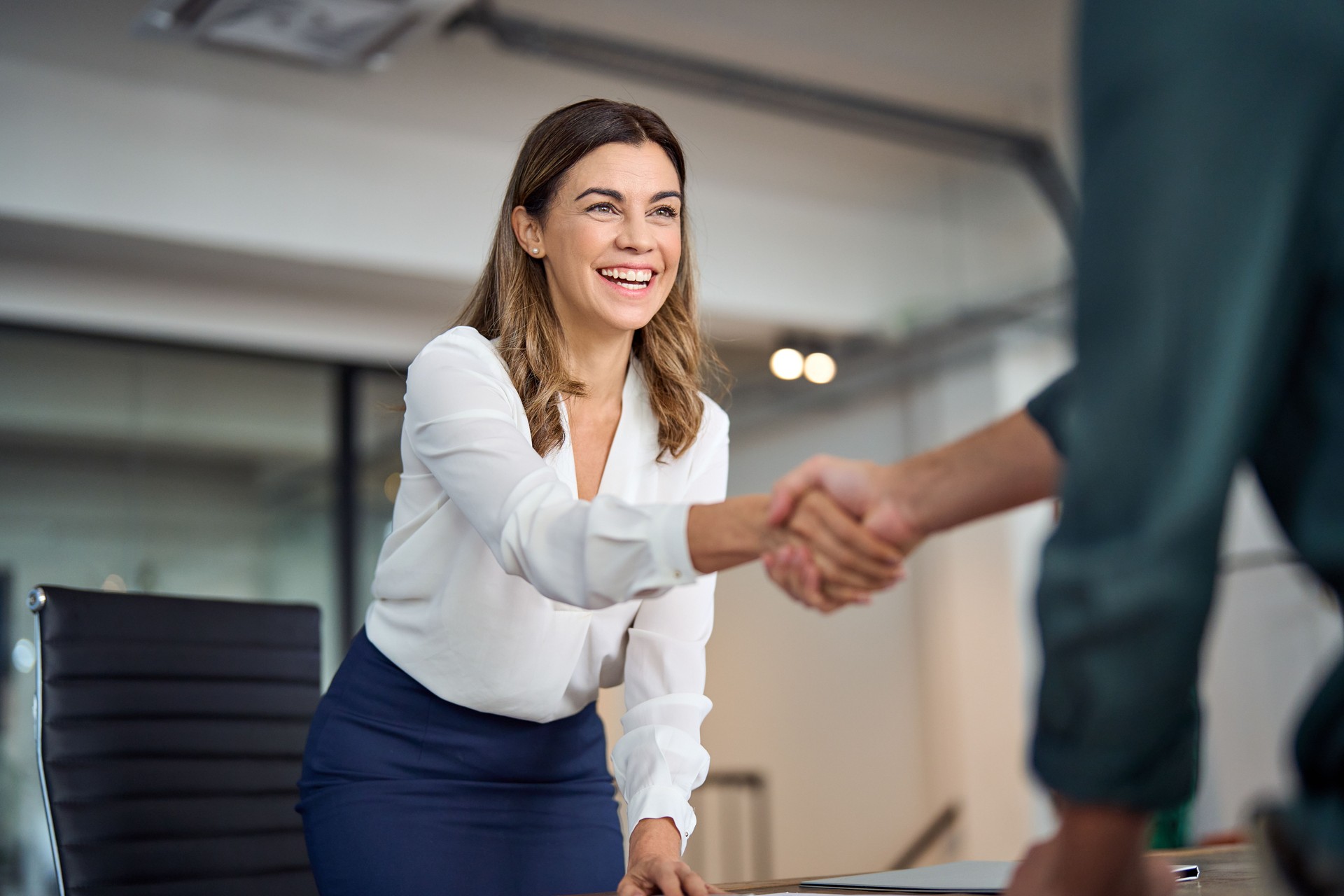 Happy mid aged business woman manager handshaking greeting client in office.